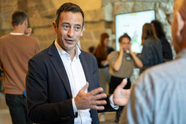Le conseiller d'Etat parle à un journaliste, debout, les mains écartées.