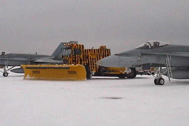 entre deux avions sur un aérodrome militaire, un engin de déneigement de cette firme, doté d'une lame chasse-neige.