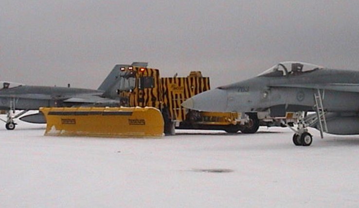 entre deux avions sur un aérodrome militaire, un engin de déneigement de cette firme, doté d'une lame chasse-neige.