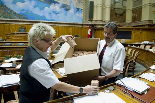 Les huissiers du Conseil national deposent des bouchons vaudois les pupitres des parlemenaires au Palais federal. Photo © ARC-Sieber