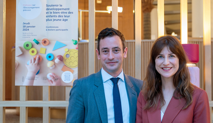 Les deux personnes posent devant une affiche du colloque pour l'encouragement précoce du 18 janvier 2024.