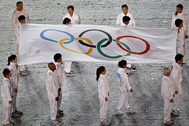 De jeunes sportifs filles et garçons vêtus en blanc portent le drapeau olympique sur de la neige.