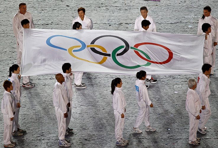 De jeunes sportifs filles et garçons vêtus en blanc portent le drapeau olympique sur de la neige.