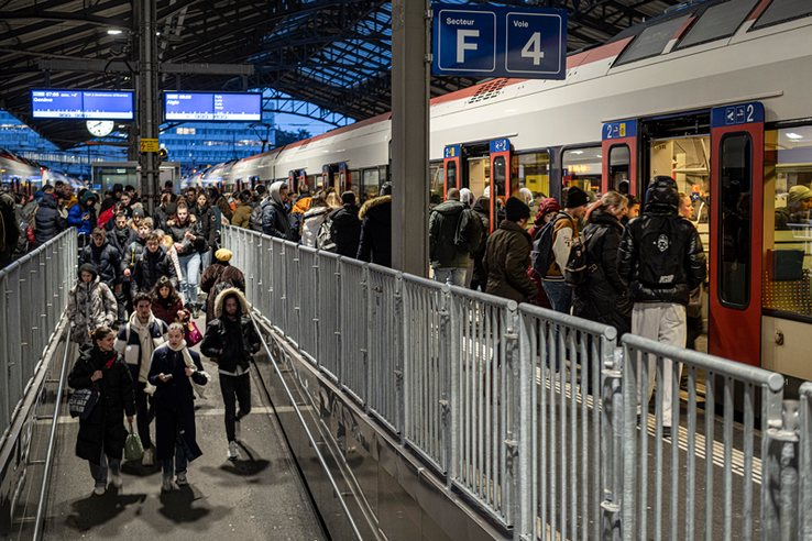 Des personnes se pressent sur un quai de la gare de Lausanne le matin tôt, des trains sont arrêtés des deux côtés du quai. Au centre, l'escalier avec ses barrières provisoires.