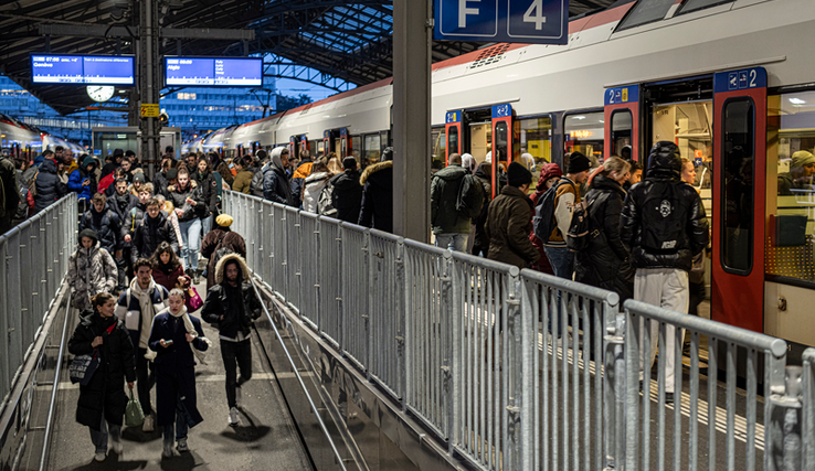 Des personnes se pressent sur un quai de la gare de Lausanne le matin tôt, des trains sont arrêtés des deux côtés du quai. Au centre, l'escalier avec ses barrières provisoires.