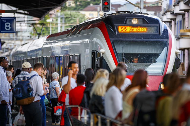 Vue d'un quai de la gare avec de nombreuses personnes voyageant. Un train à destination de Grandson est à quai.