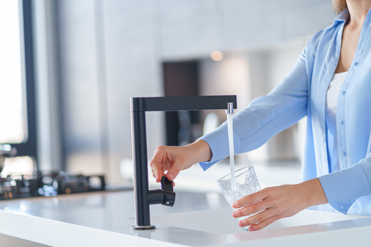 une femme remplit un verre d'eau au robinet d'une cuisine
