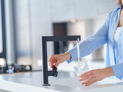 une femme remplit un verre d'eau au robinet d'une cuisine