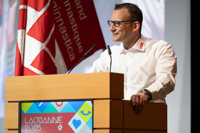 La personne à la tribune, en train de parler. Derrière, le drapeau de la manifestation.