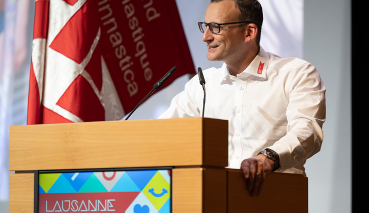 La personne à la tribune, en train de parler. Derrière, le drapeau de la manifestation.